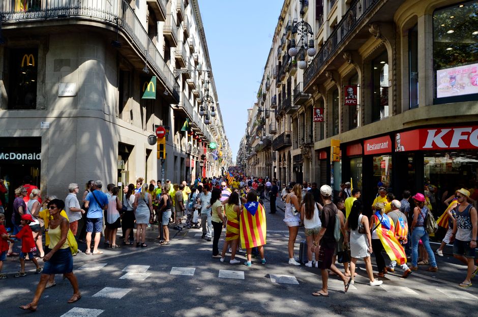 Calle concurrida en Barcelona con una multitud diversa mostrando banderas catalanas y estilo de vida urbano.