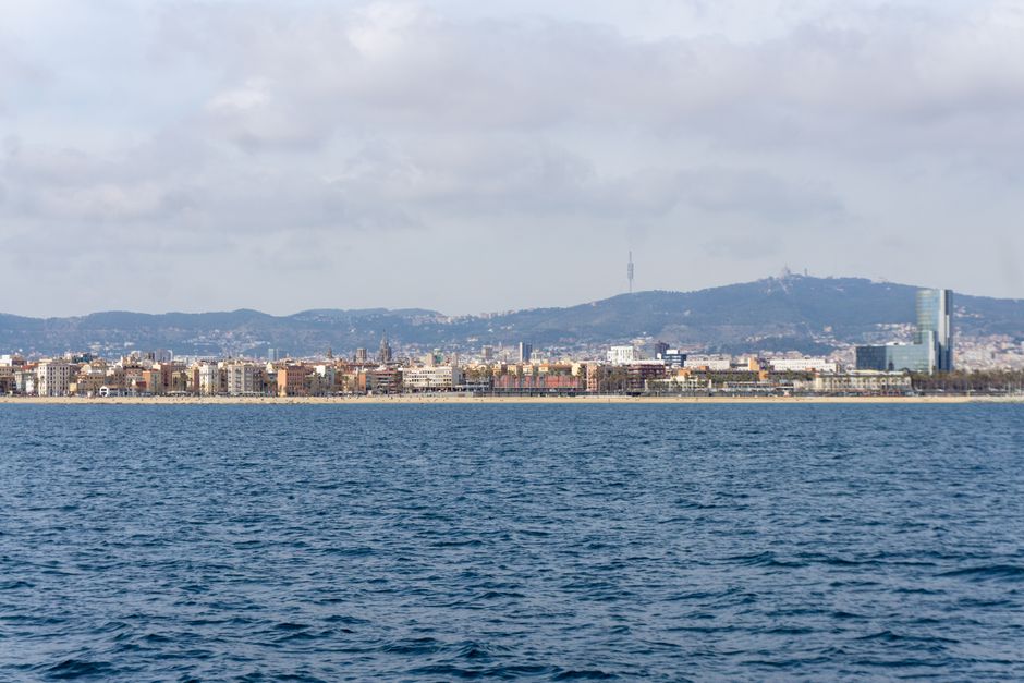 Impresionante vista panorámica de la costa de Barcelona con el skyline urbano y colinas distantes bajo un cielo nublado.