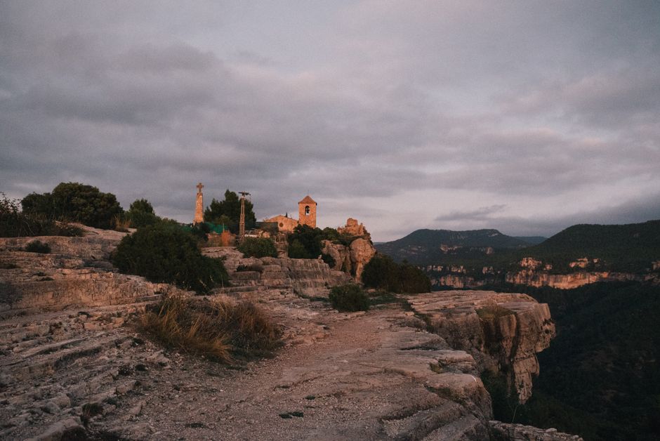 Vista escénica de una iglesia rural y una cruz en el borde de un acantilado con cielos dramáticos al atardecer.