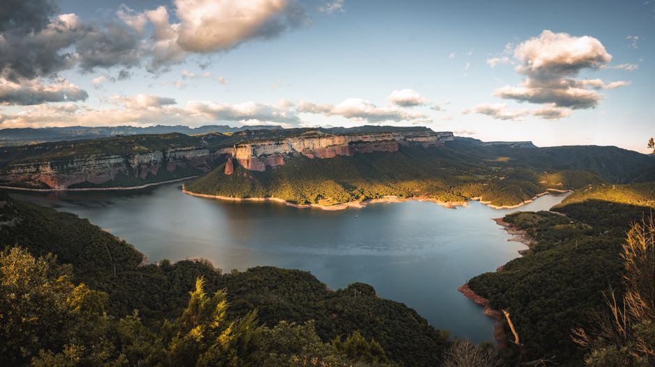 Una impresionante vista aérea de una presa en un paisaje montañoso bajo un cielo parcialmente nublado.