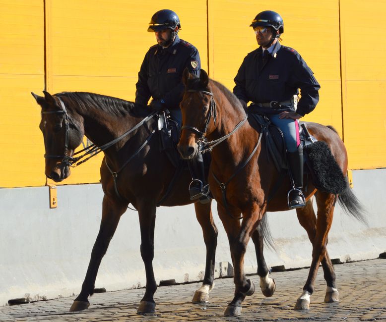 Dos agentes de policía montados a caballo junto a la pared amarilla de un edificio.