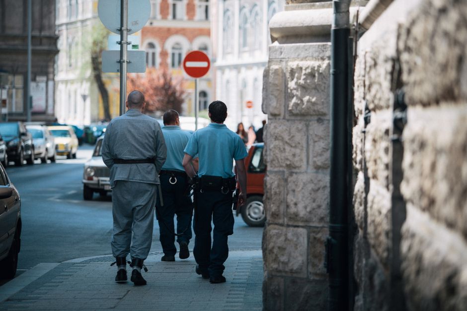 Los policías escortan a un prisionero con grilletes por una calle de la ciudad, mostrando la aplicación de la ley en acción.