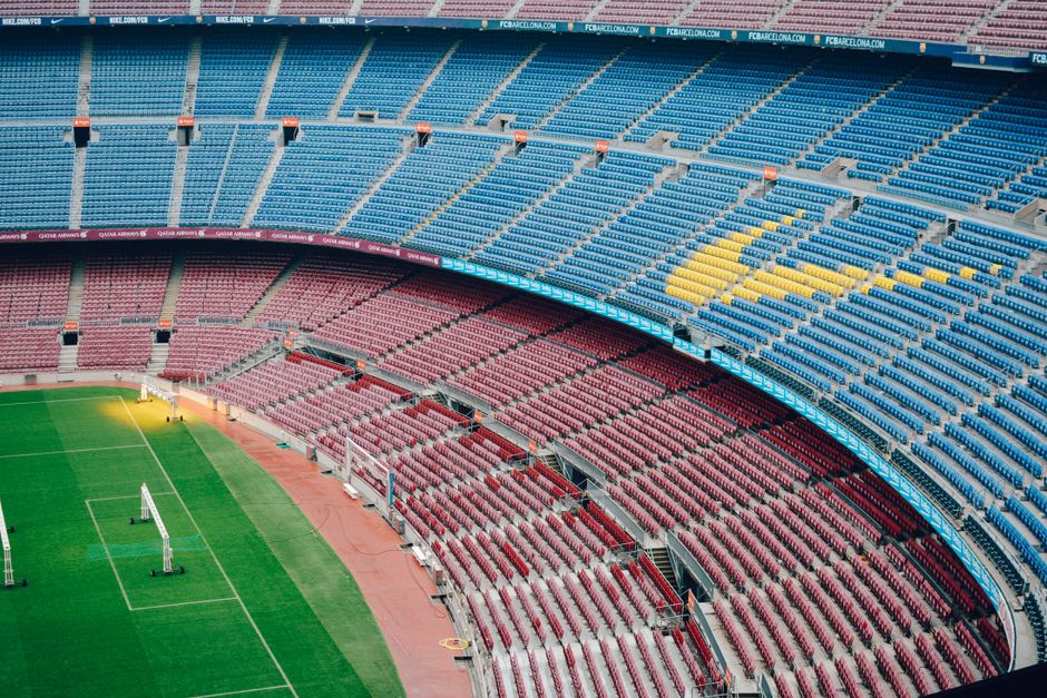Vista aérea del estadio vacío Camp Nou en Barcelona con asientos coloridos y campo verde.