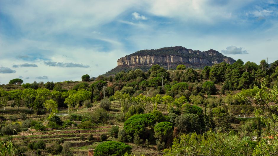 Impresionante vista del exuberante paisaje de Gallifa con la montaña prominente de fondo bajo un cielo brillante.