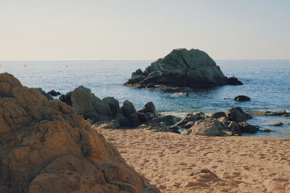 Pintoresca escena de playa en la Costa Brava con aguas cristalinas y destacadas formaciones rocosas.