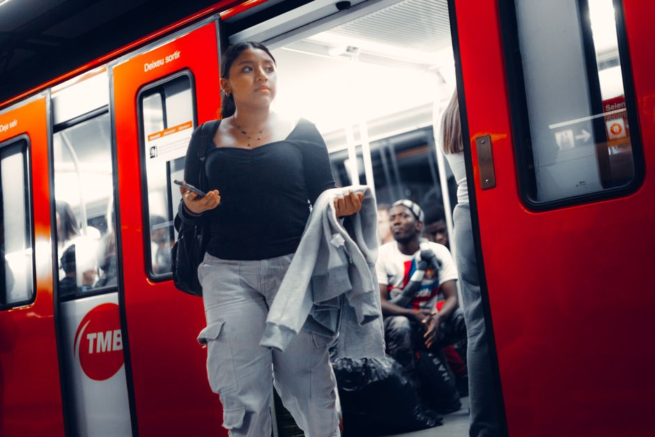 Mujer sale de un tren rojo brillante en una concurrida plataforma de metro de la ciudad sosteniendo un teléfono inteligente.