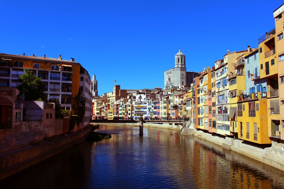 Escena cautivadora de las coloridas casas emblemáticas de Girona a lo largo del río Onyar bajo un cielo azul claro.