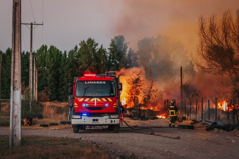 Bomberos en acción combatiendo un incendio forestal descontrolado cerca de una zona rural con un camión de bomberos visible.