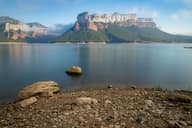 Escena tranquila del Embalse de Sau con majestuosas montañas bajo cielos claros.