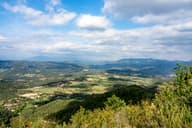 Descubre el exuberante paisaje de Alpens con colinas onduladas y valles verdes vibrantes bajo un cielo brillante.