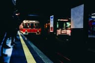 Escena urbana nocturna de un tren llegando a una estación de metro en Milán, capturando movimiento y vida de la ciudad.