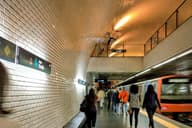 Viajeros caminando por una plataforma concurrida del metro de Lisboa con un tren en movimiento.