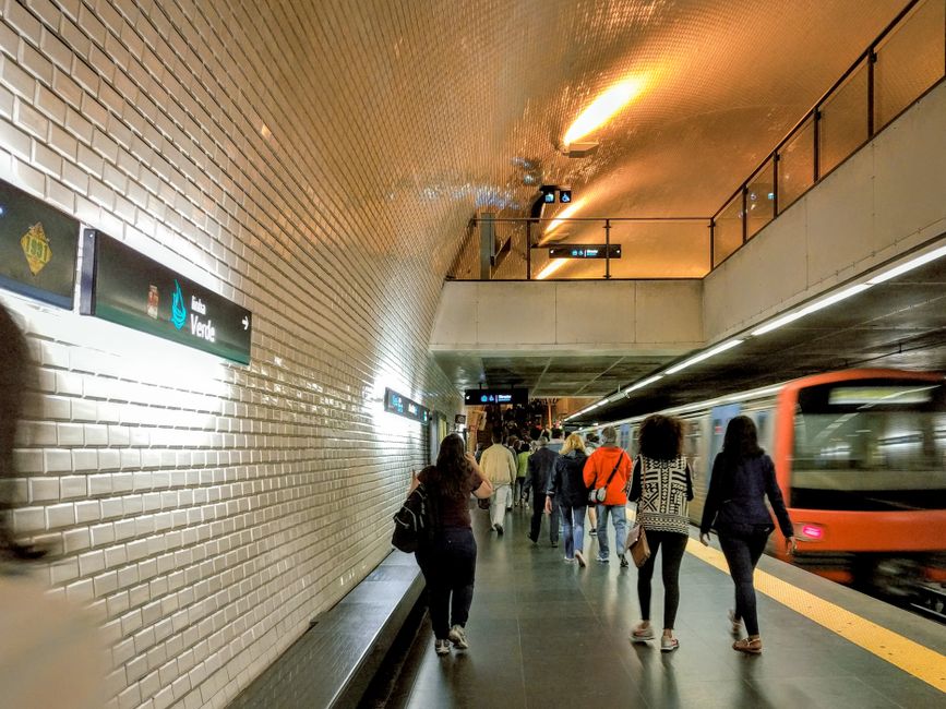 Viajeros caminando por una plataforma concurrida del metro de Lisboa con un tren en movimiento.