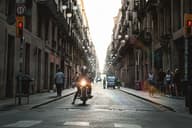 Un motociclista recorre una calle histórica soleada en Barcelona, España, capturando la vida urbana.