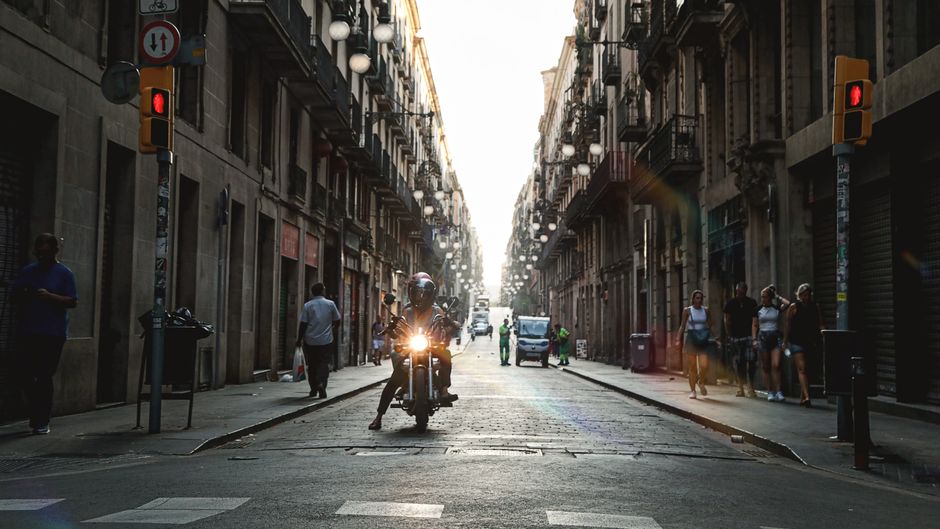 Un motociclista recorre una calle histórica soleada en Barcelona, España, capturando la vida urbana.