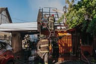 Bomberos trabajando para extinguir un incendio en una casa, mostrando valentía y trabajo en equipo al aire libre.