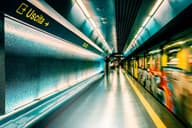 Escena dinámica de una estación de metro en Nápoles con un tren en movimiento y señalización iluminada.