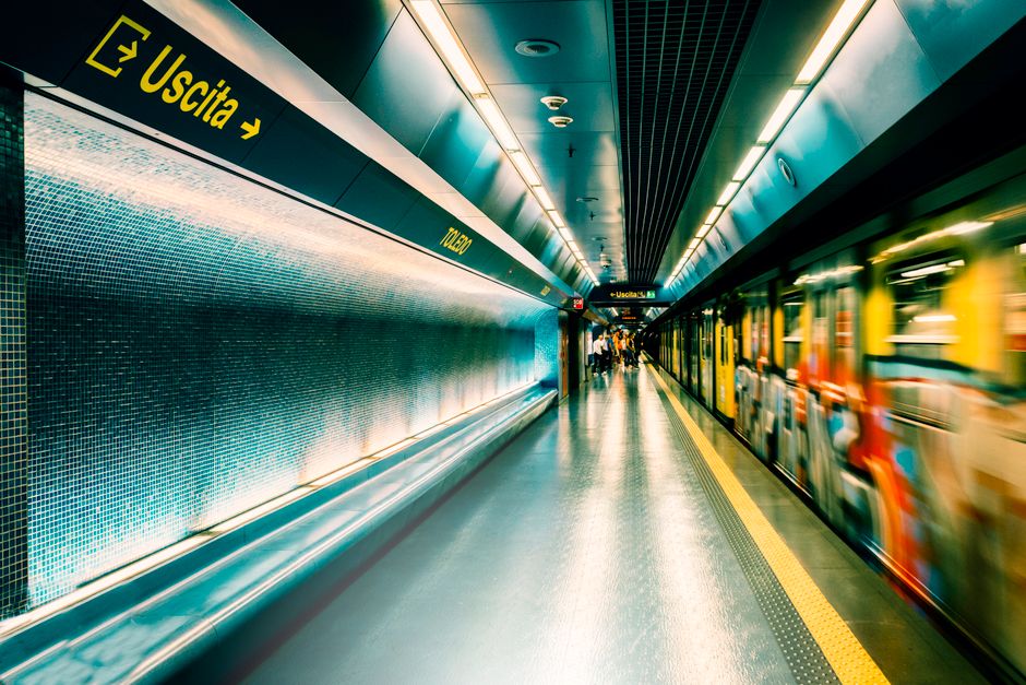 Escena dinámica de una estación de metro en Nápoles con un tren en movimiento y señalización iluminada.