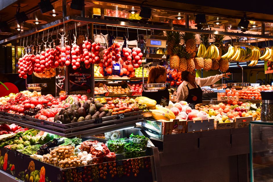 Puesto colorido de frutas en el Mercado de La Boqueria, Barcelona, exhibiendo productos frescos bajo luces cálidas.
